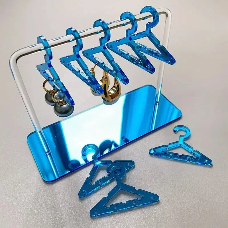 Rangement pour bijoux bleu avec cintres miniatures translucides, posé sur une base miroir bleutée pour une touche moderne et stylée.