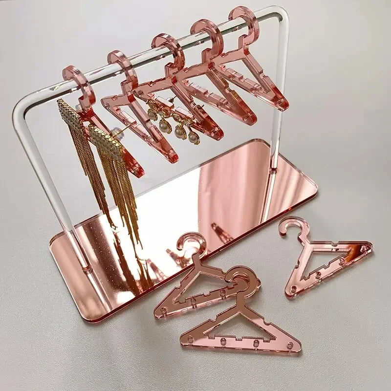 Rangement pour bijoux rose poudré avec cintres assortis, exposant délicatement les boucles d’oreilles dans un décor doux et féminin.