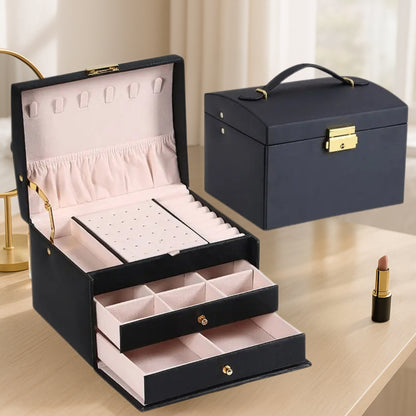 Boite à bijoux noire élégante posée sur une coiffeuse en bois clair, avec intérieur en velours et bijoux bien organisés dans les compartiments.