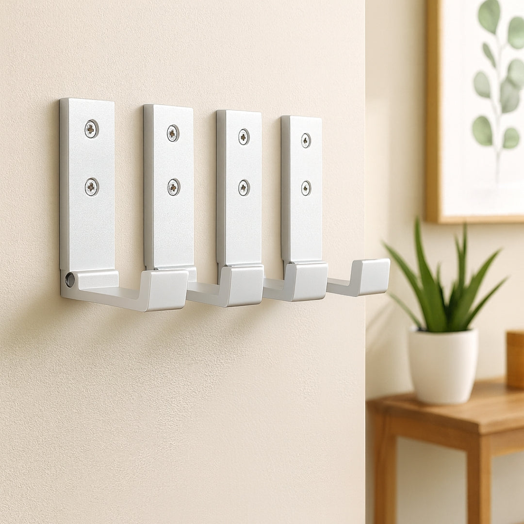 Quatre crochets muraux rabattables argent alignés sur un mur beige, style épuré et fonctionnel.