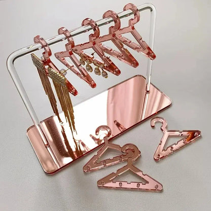 Rangement pour bijoux rose poudré avec cintres assortis, exposant délicatement les boucles d’oreilles dans un décor doux et féminin.